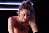 A young woman wearing a peach coloured top and shorts pedalling on an exercise bike in a gym.