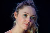 A young woman wearing a peach coloured crop top facing the camera in front of a black background.