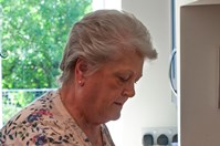 A woman (Anna) in a white, flowery top, standing in front of a hob in a kitchen. She is using tongs to turn over chicken strips which are cooking in a wok.