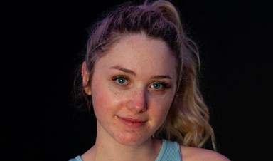 A young woman wearing a pale blue top and shorts, facing the camera with her arms folded and smiling slightly.